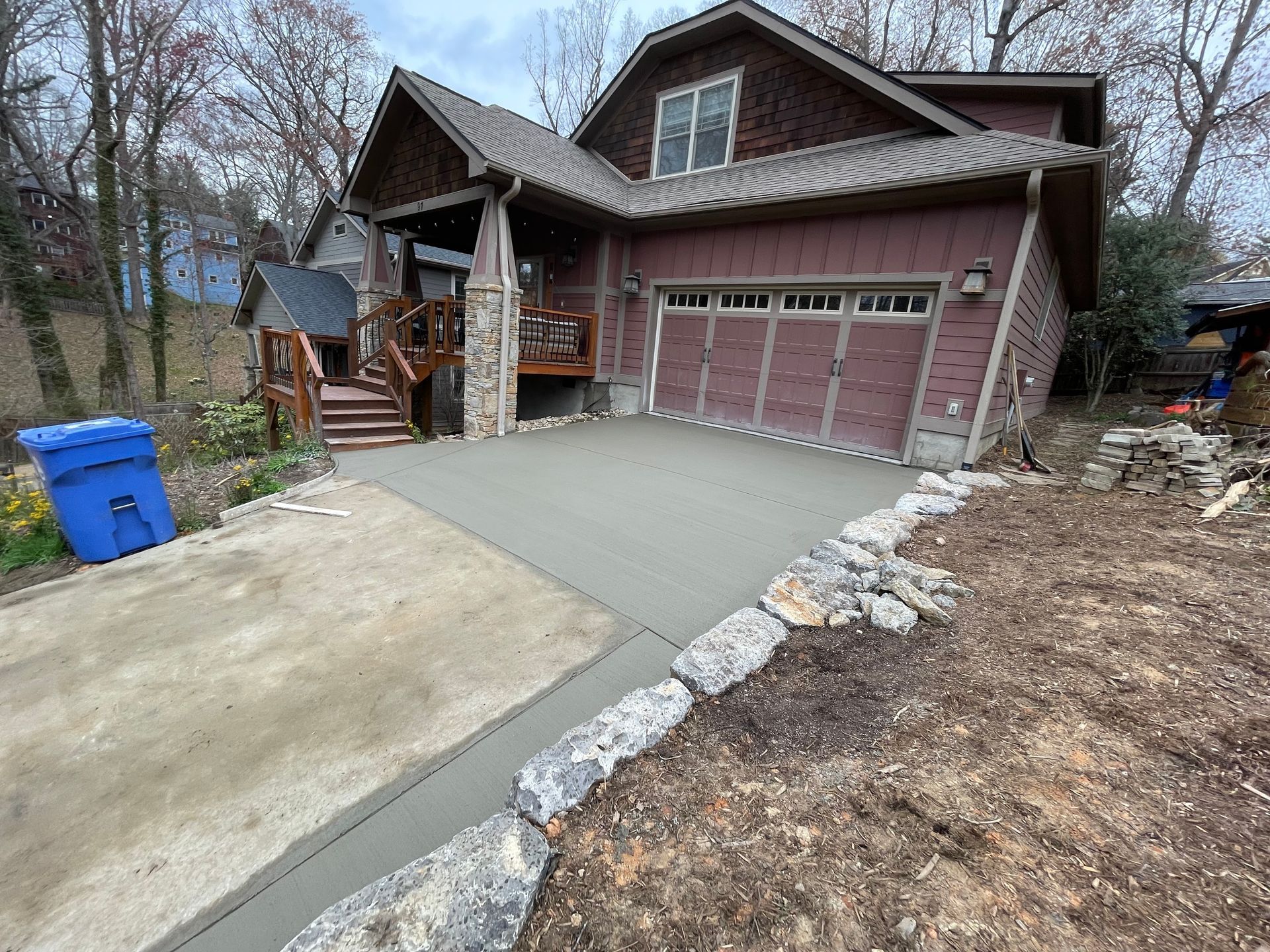A newly poured concrete driveway leads to a two-car garage attached to a brown house with stone pillar accents.