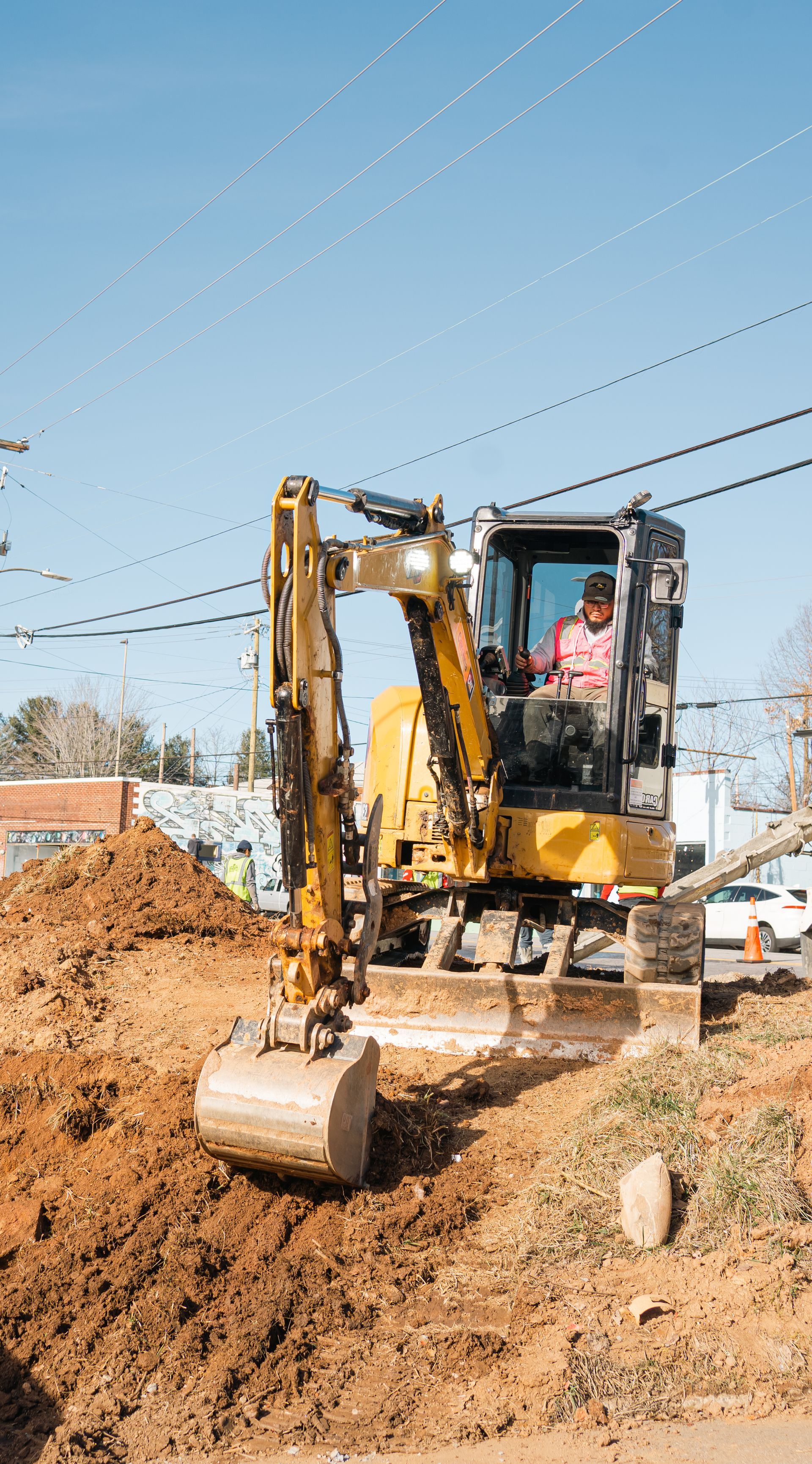 A yellow excavator operating in a dirt-filled construction site under a clear blue sky.