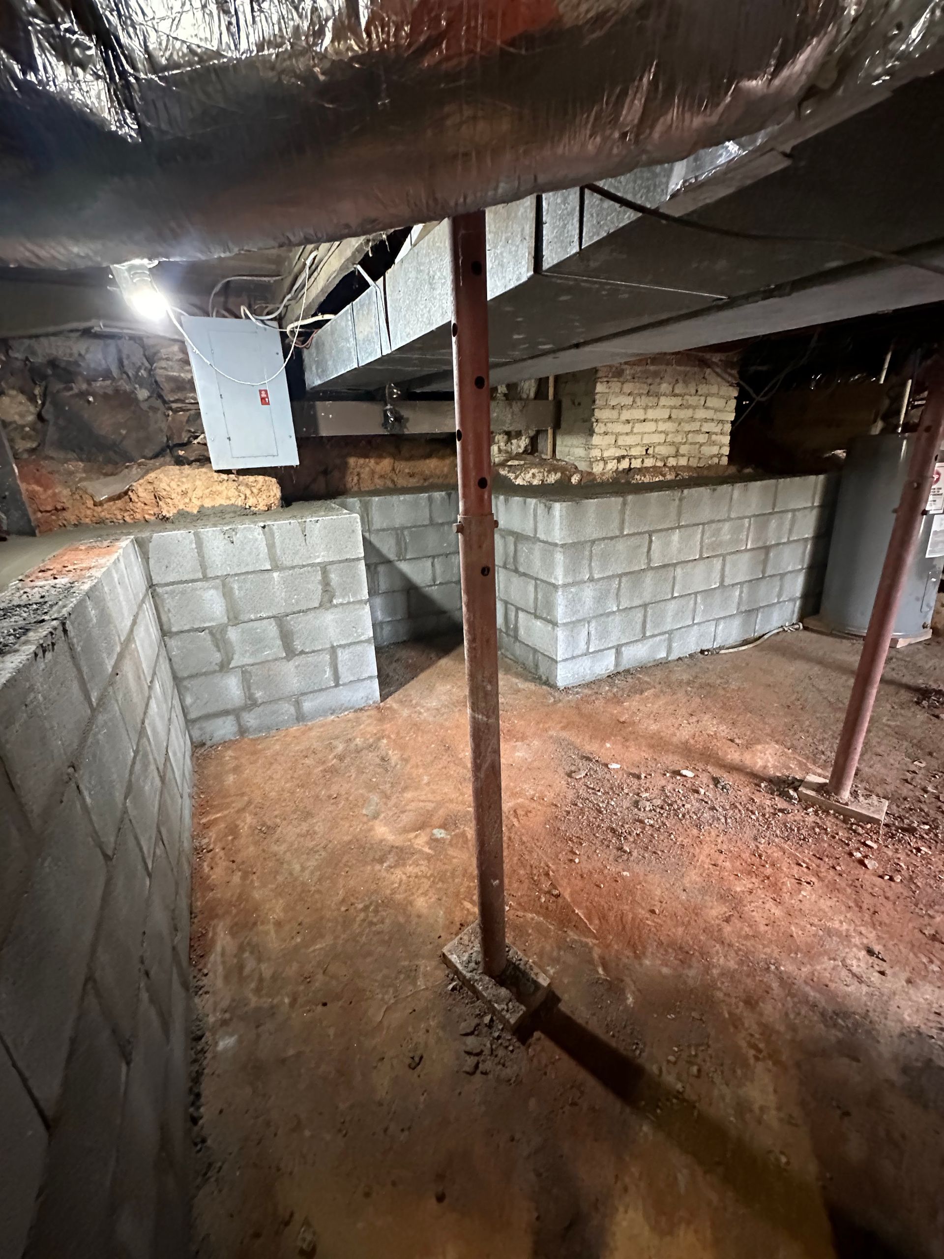 A basement crawlspace features new gray concrete block walls, exposed joists, and vertical metal support columns.