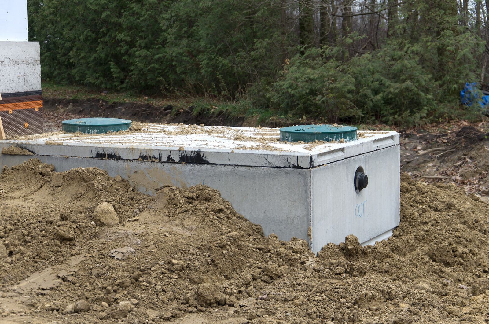 Concrete septic tank surrounded by dirt at a wooded construction site