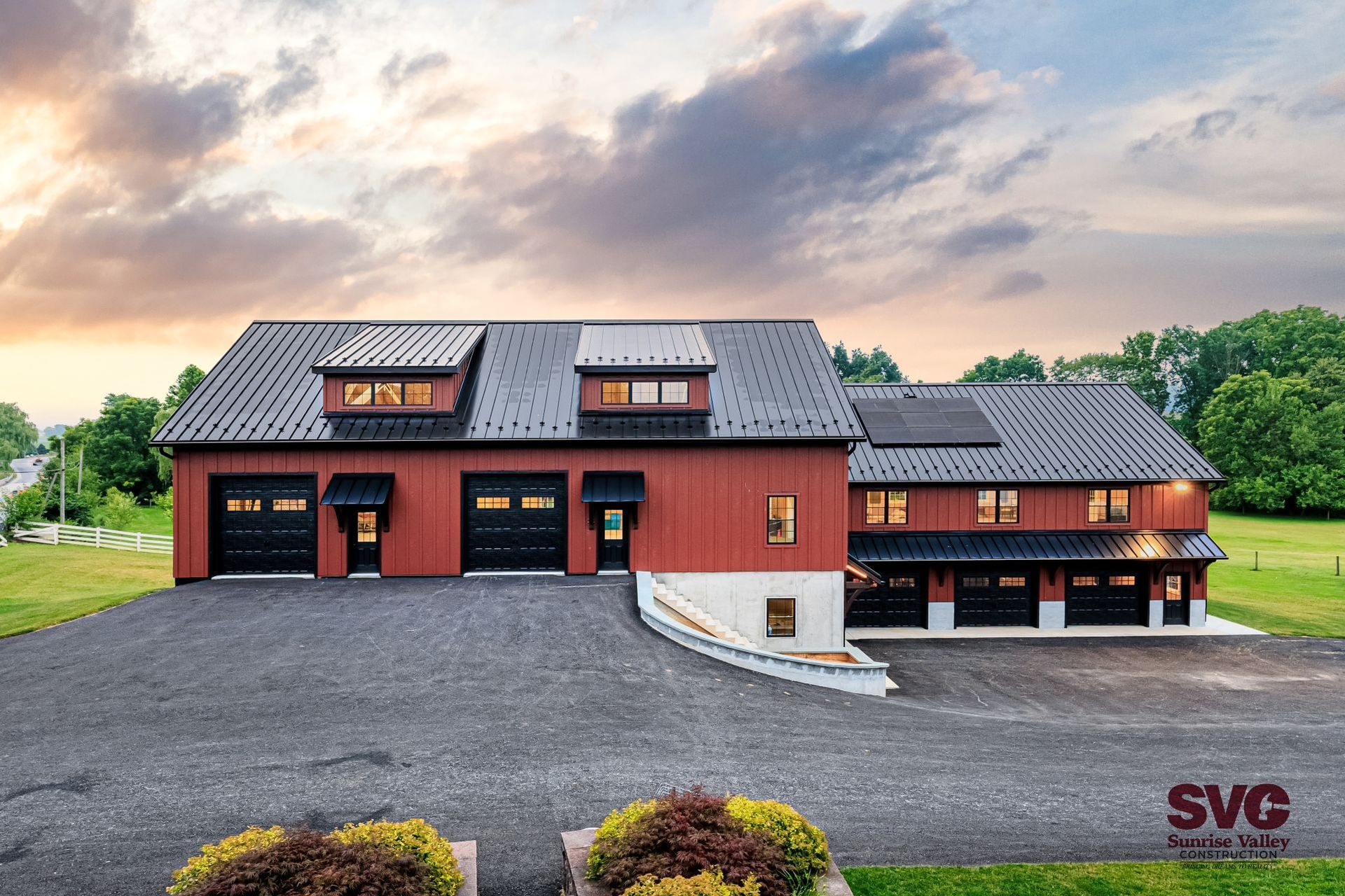 Red bank barn with black metal roof, 5 black garage doors, and lighted interior 