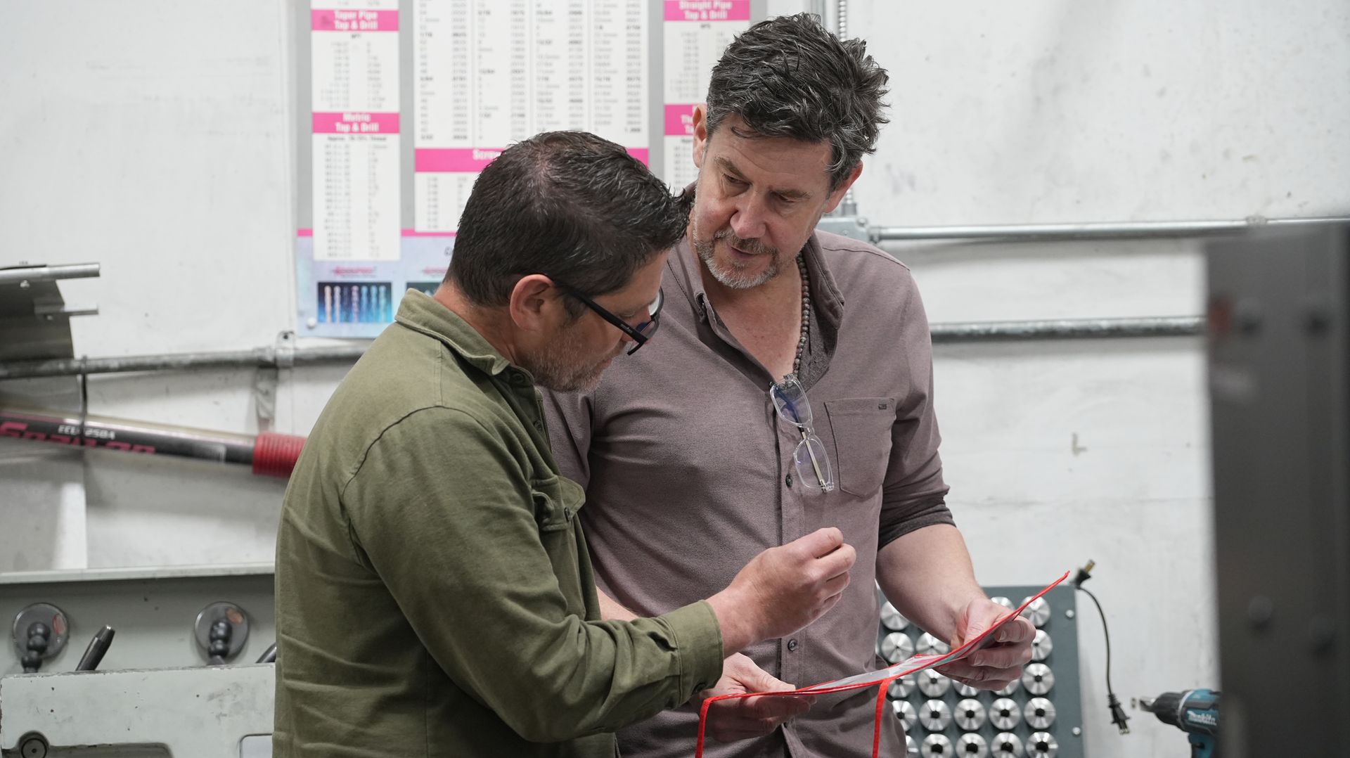 A man is working on a machine in a factory while holding a book.