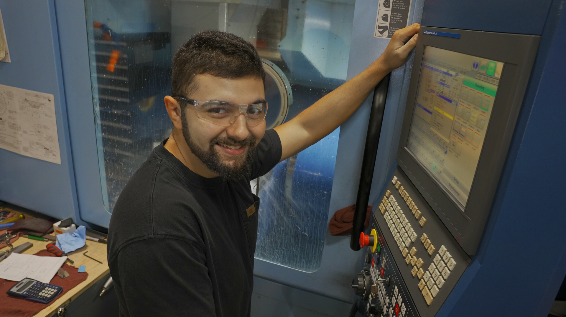 A man with a beard is standing in front of a machine.