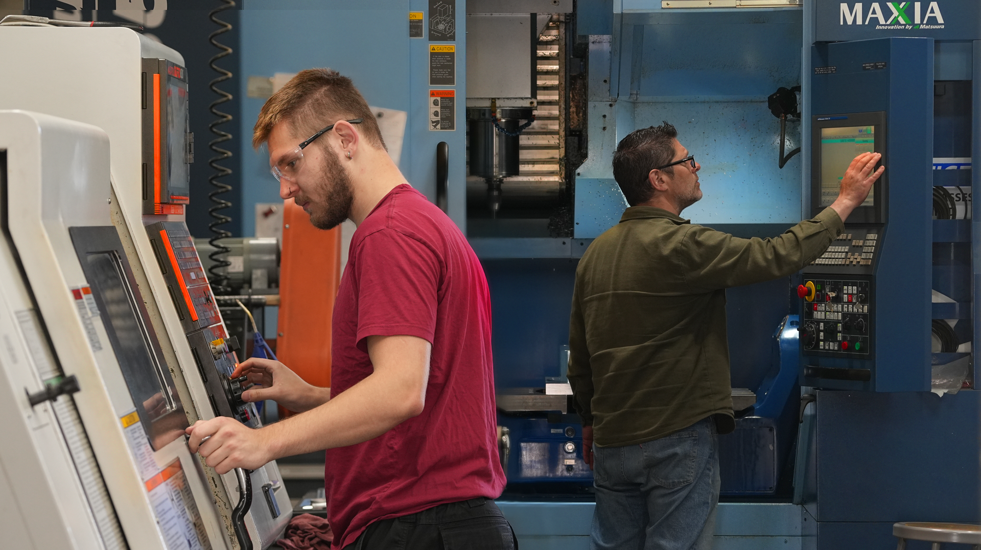 Two machinists in the Atlas factory, one wearing red, another wearing green.