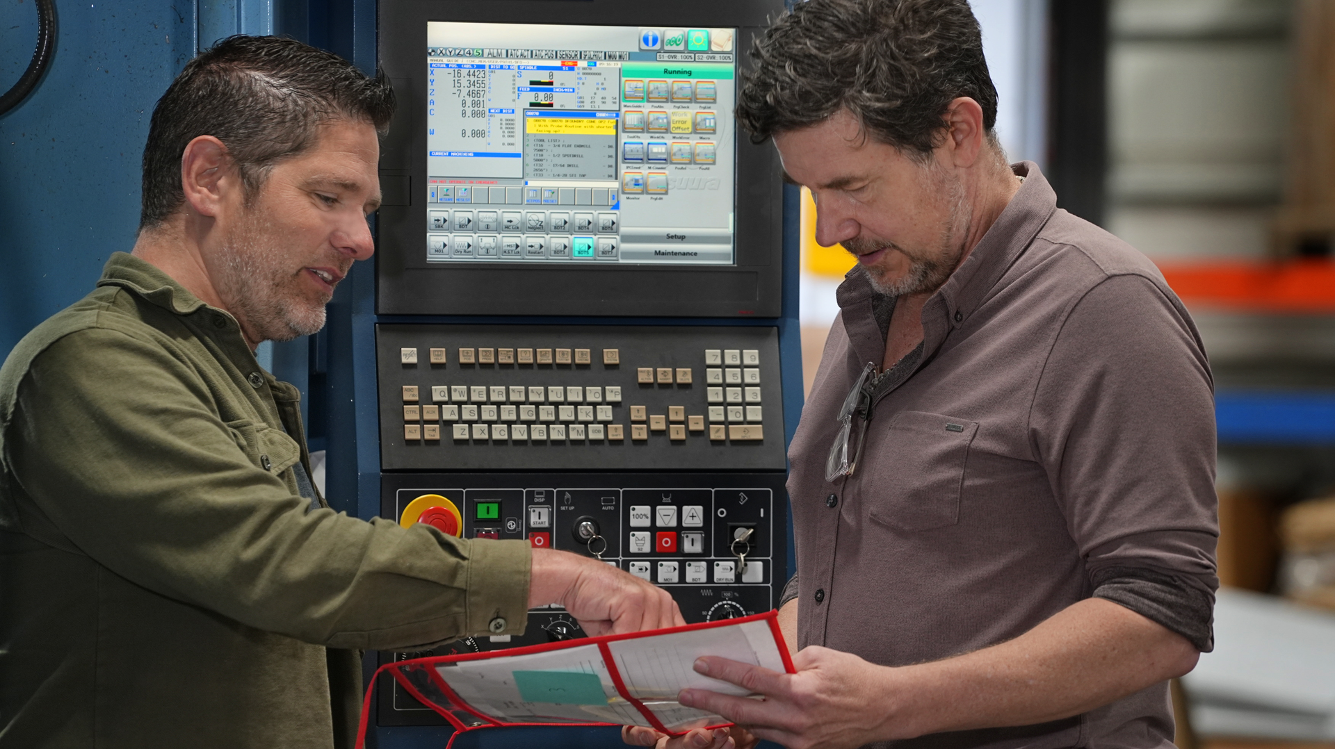 Atlas machinist and Atlas owner/engineer discussing a job folder in front of a CNC control panel.