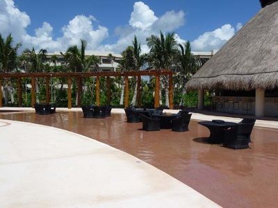 A swimming pool with chairs and tables and a thatched roof