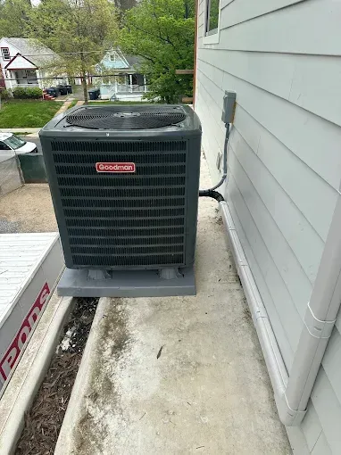 Goodman air conditioning unit on a concrete pad next to a house with white siding and a downspout.