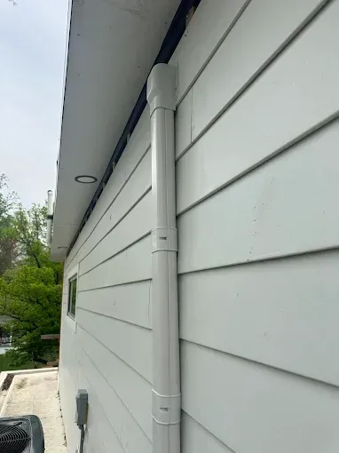 White siding on a building with a white downspout running vertically along the wall.