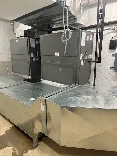 HVAC units and metal ductwork in an indoor setting. Gray units mounted above galvanized steel ducts.