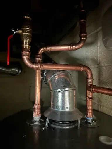 Copper pipes connected to a water heater and flue. Fittings and a red handled valve are visible.