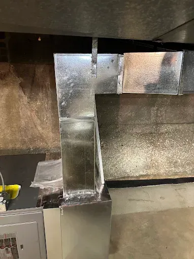 Galvanized metal ductwork connected to an HVAC unit in a basement setting.