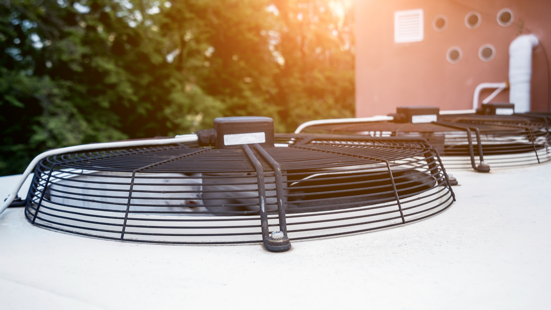 Two black air conditioning unit fans atop a building, sunlight in the background.
