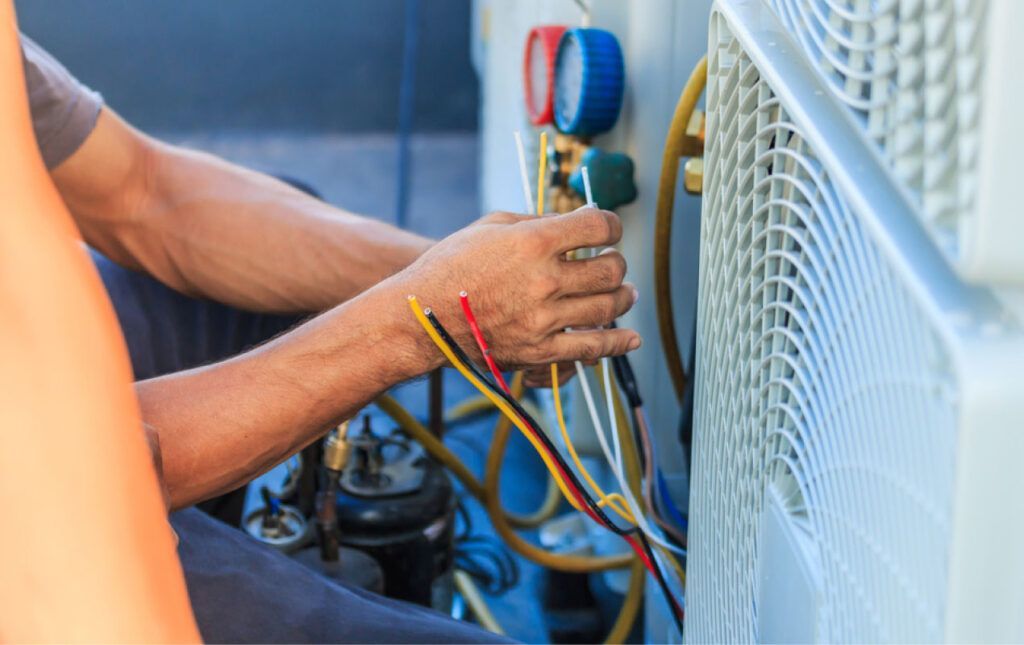 A technician holding colored electrical wires while repairing the external unit of an air conditioning system.
