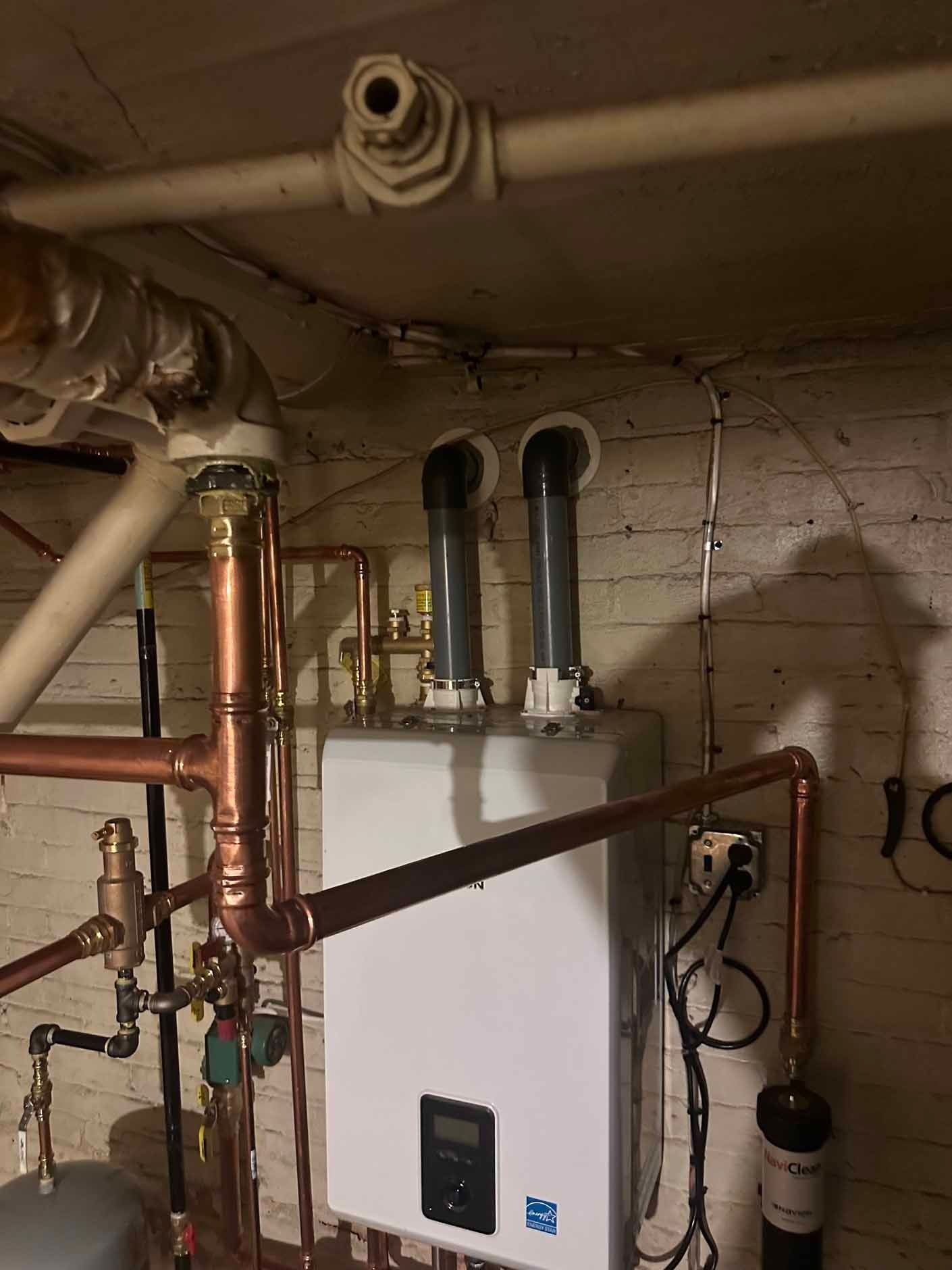 A wall-mounted white water heater with copper pipes in a basement setting.