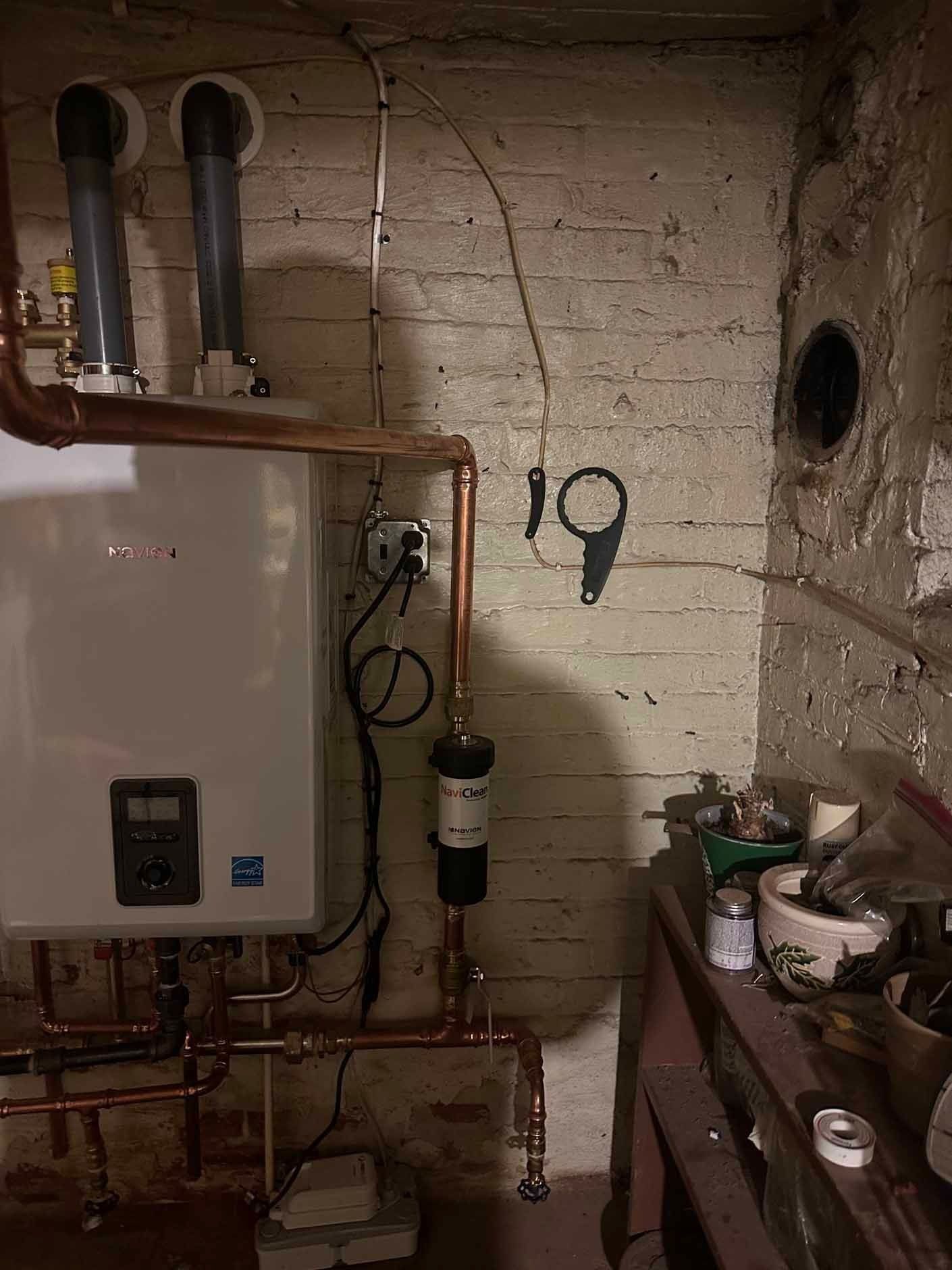 White water heater with copper pipes in a brick basement.