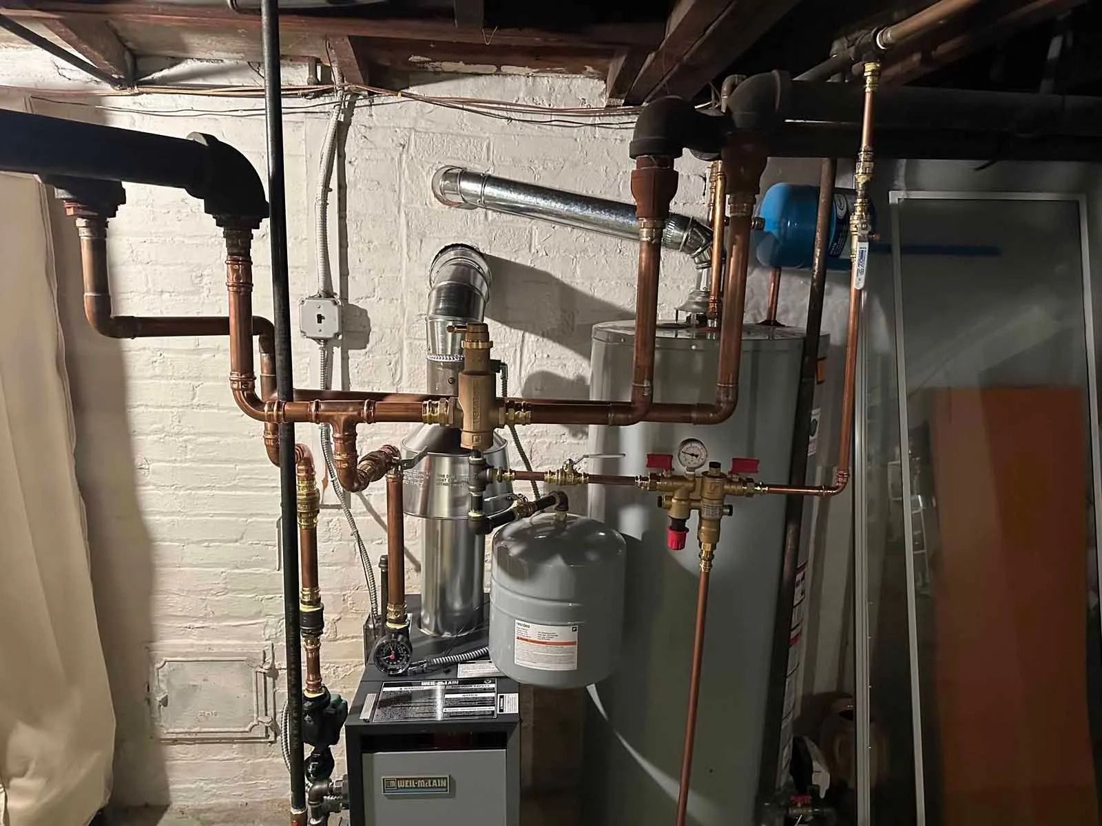 Copper pipes and a water heater against a white wall in a basement.