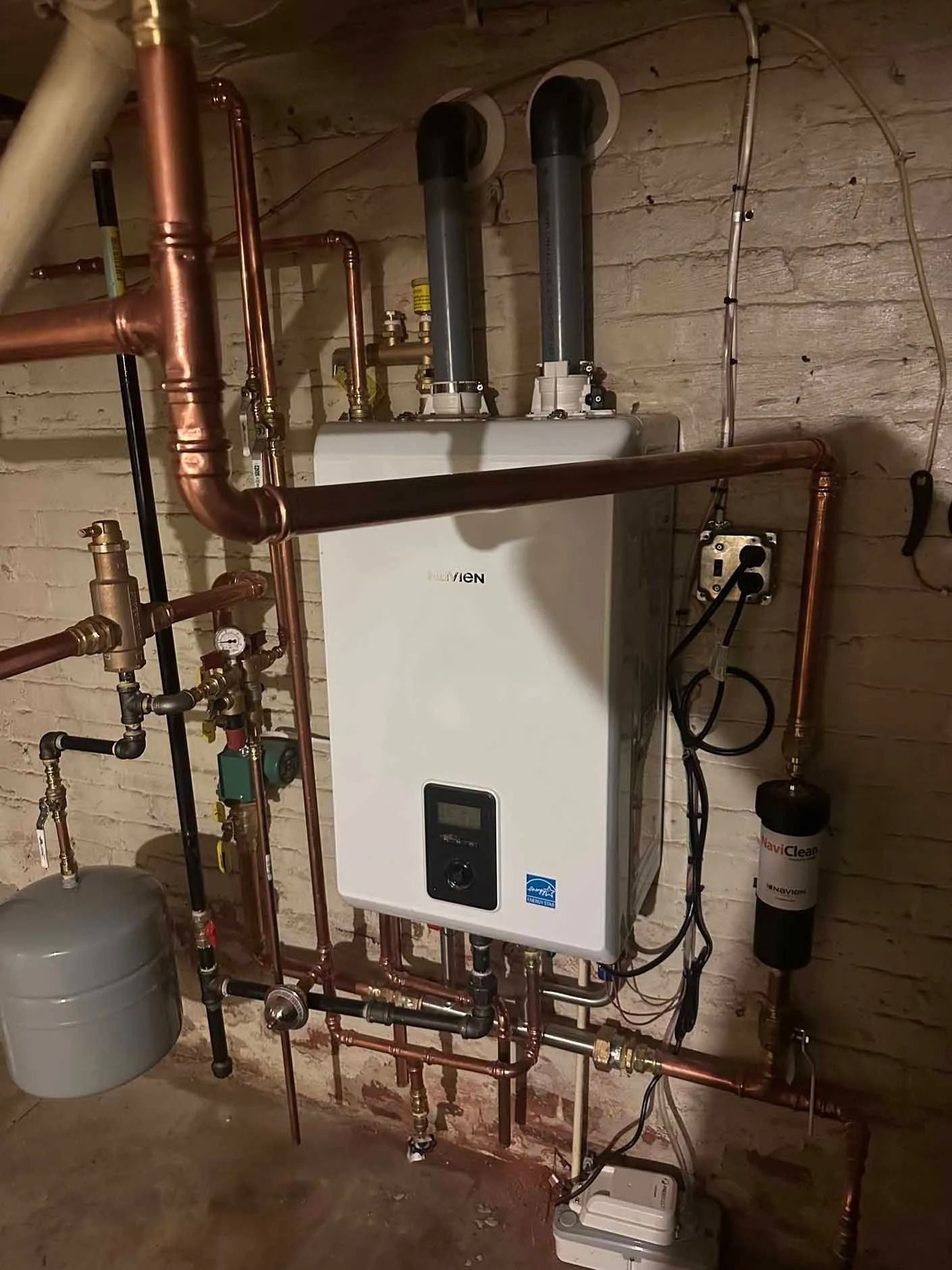 White wall-mounted water heater with copper pipes in a basement setting.
