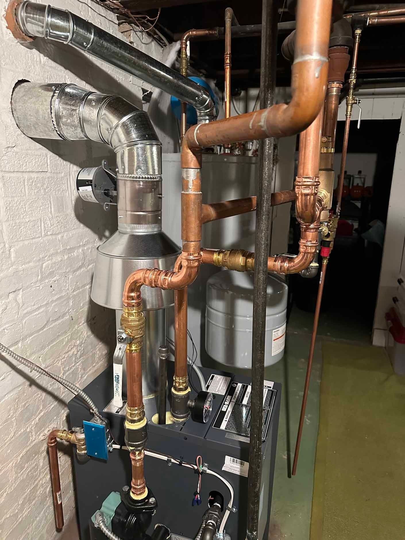 A complex plumbing system with copper pipes, a gray boiler, and metal vents in a basement.