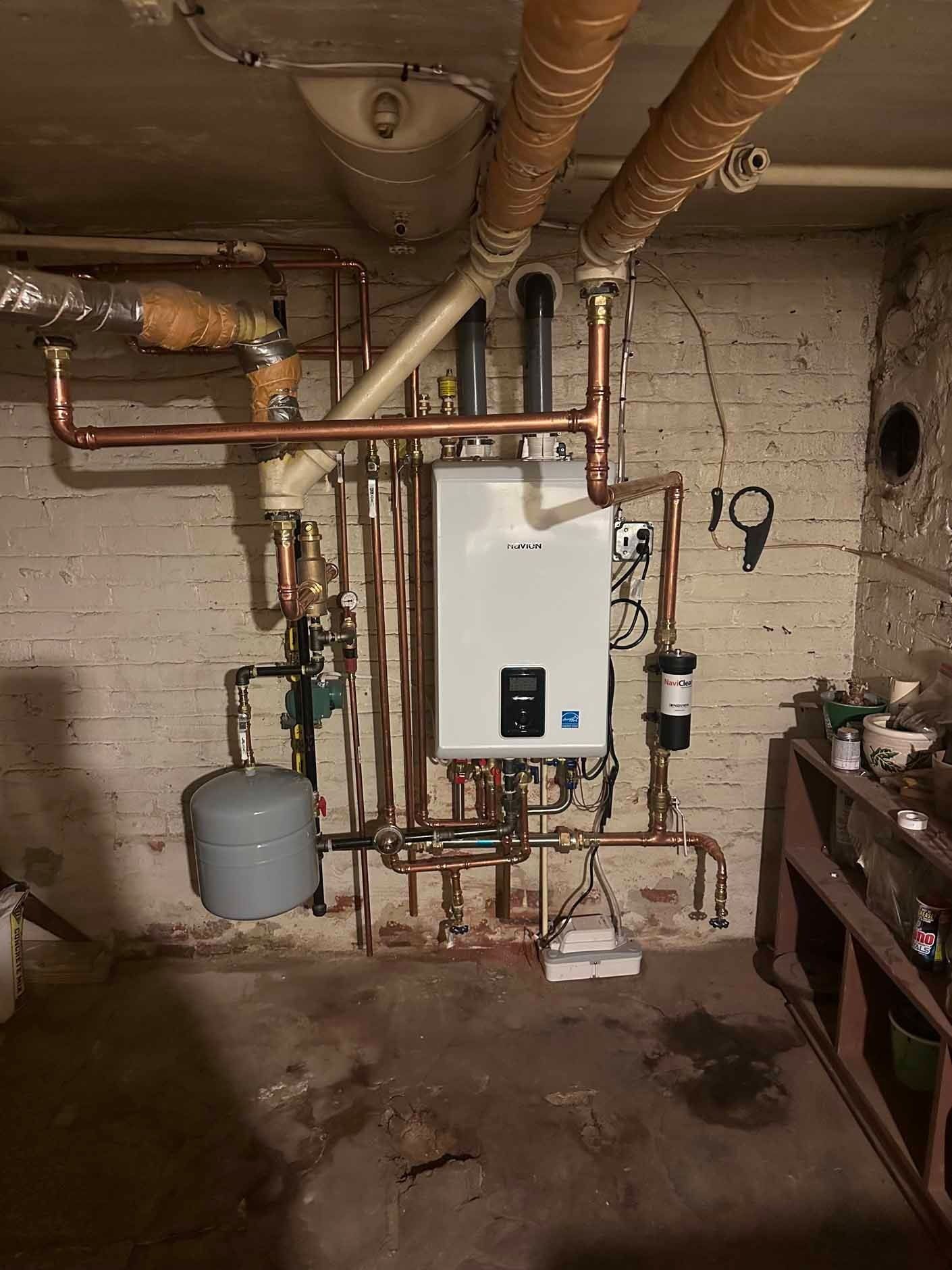 A newly installed tankless water heater with copper pipes in a basement.