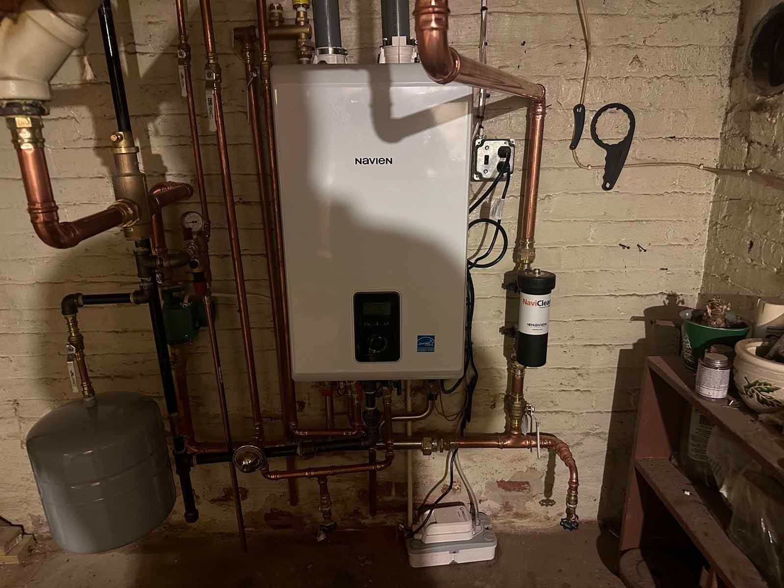 Copper pipes and a white water heater mounted on a brick wall in a basement.