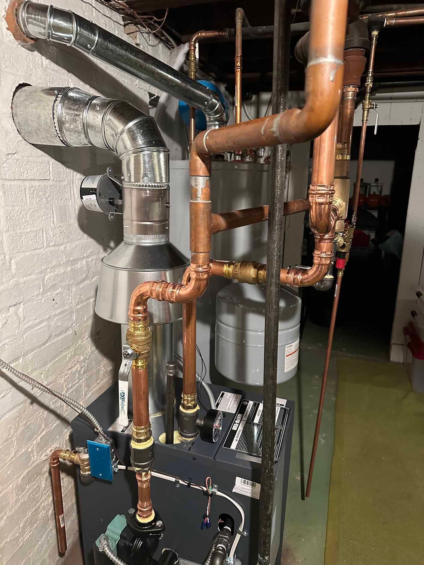 Copper pipes and vents connected to a gray boiler in a basement.