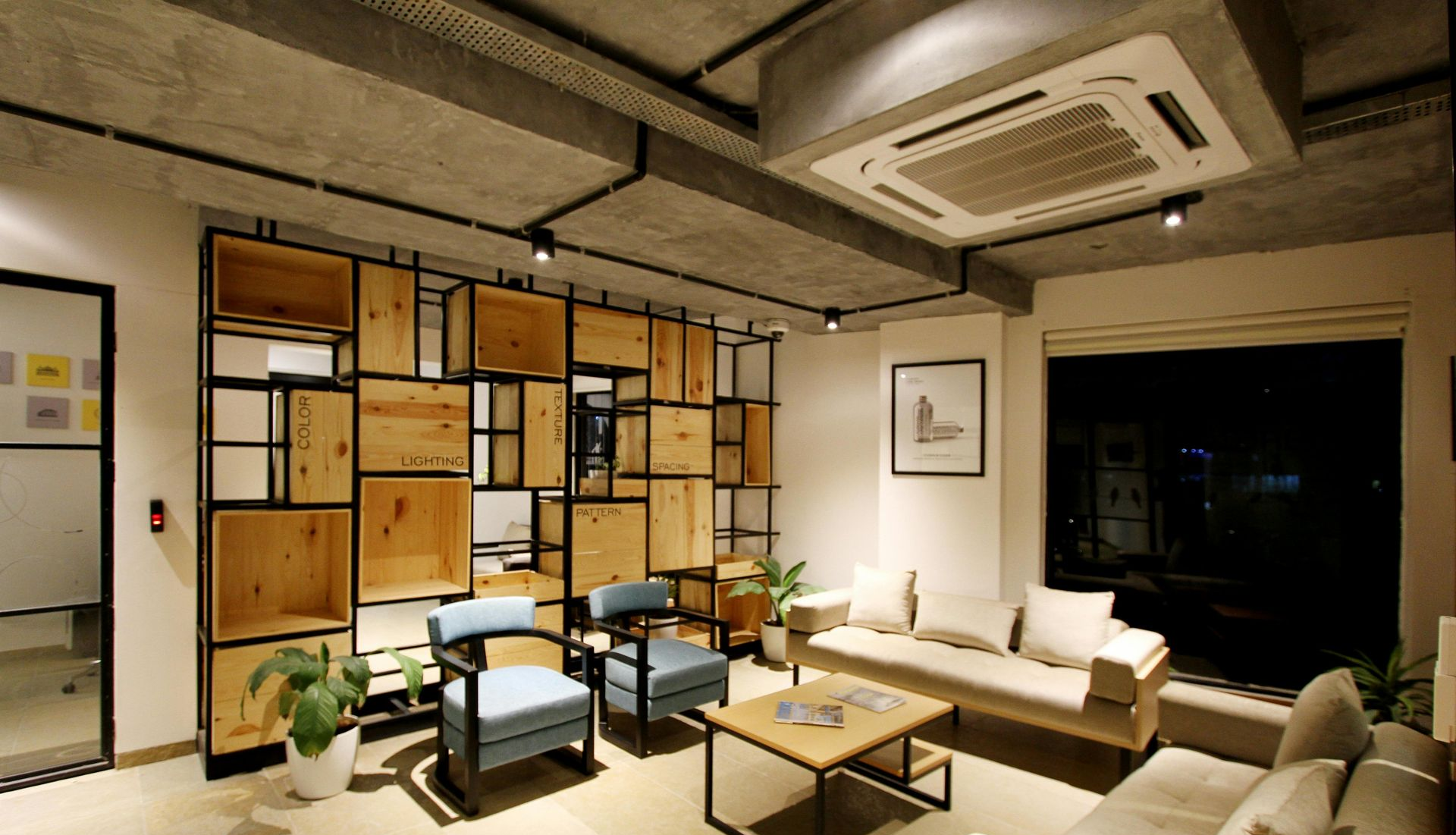Modern office lounge with wooden shelving, sofas, chairs, and potted plants.