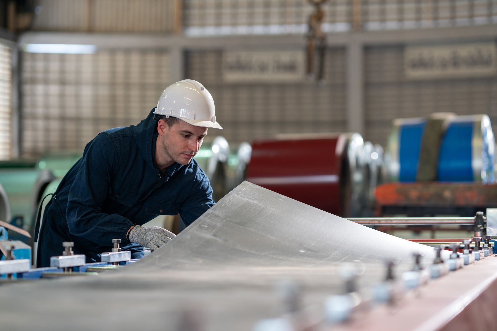 Worker in protective gear handling a large sheet on a metal fabrication machine in a factory.