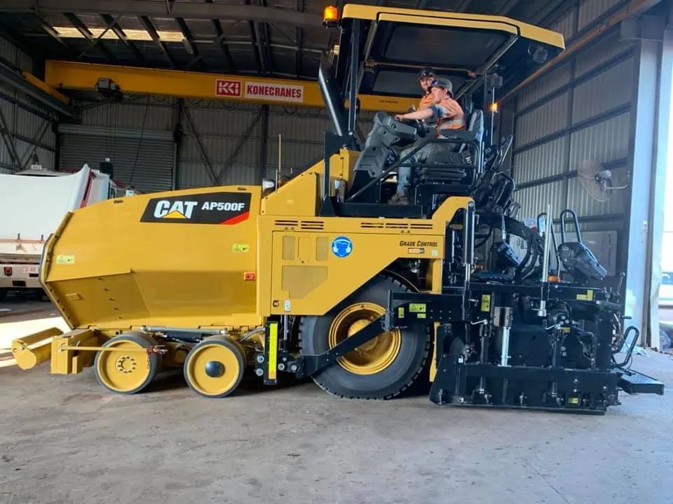 A Man is Driving a Cat Asphalt Paving Machine in a Garage — F & J Bitumen Services in Humpty Doo, NT