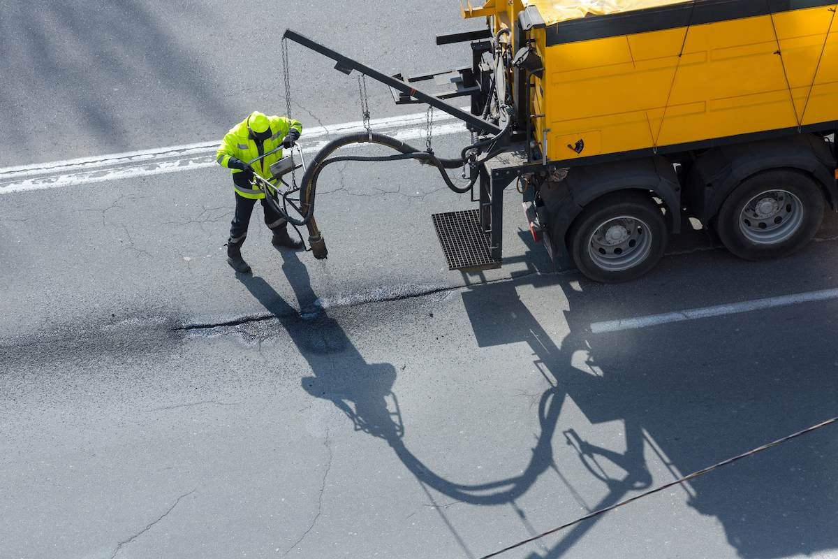 A Man is Working on the Road Next to a Yellow Truck — F & J Bitumen Services in Humpty Doo, NT
