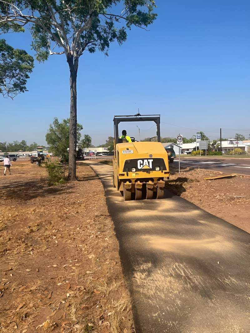 A Yellow Cat Roller is Driving Down a Dirt Road — F & J Bitumen Services in Humpty Doo, NT