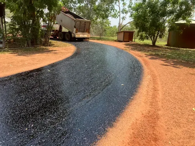 A Tip Truck Spreading Bitumen on a Dirt Road — F & J Bitumen Services in Adelaide River, NT