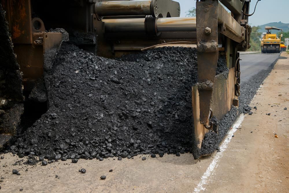 A Machine is Spreading Asphalt on the Side of a Road — F & J Bitumen Services in Alice Springs, NT