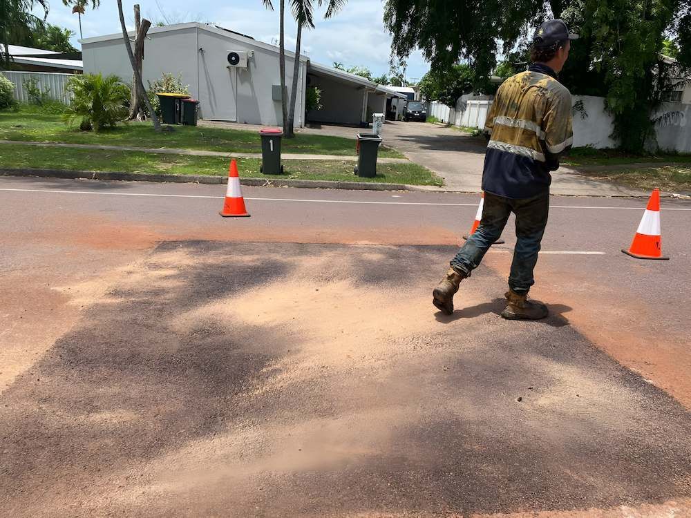 A Man is Standing in the Middle of a Street Surrounded by Traffic Cones — F & J Bitumen Services in Humpty Doo, NT