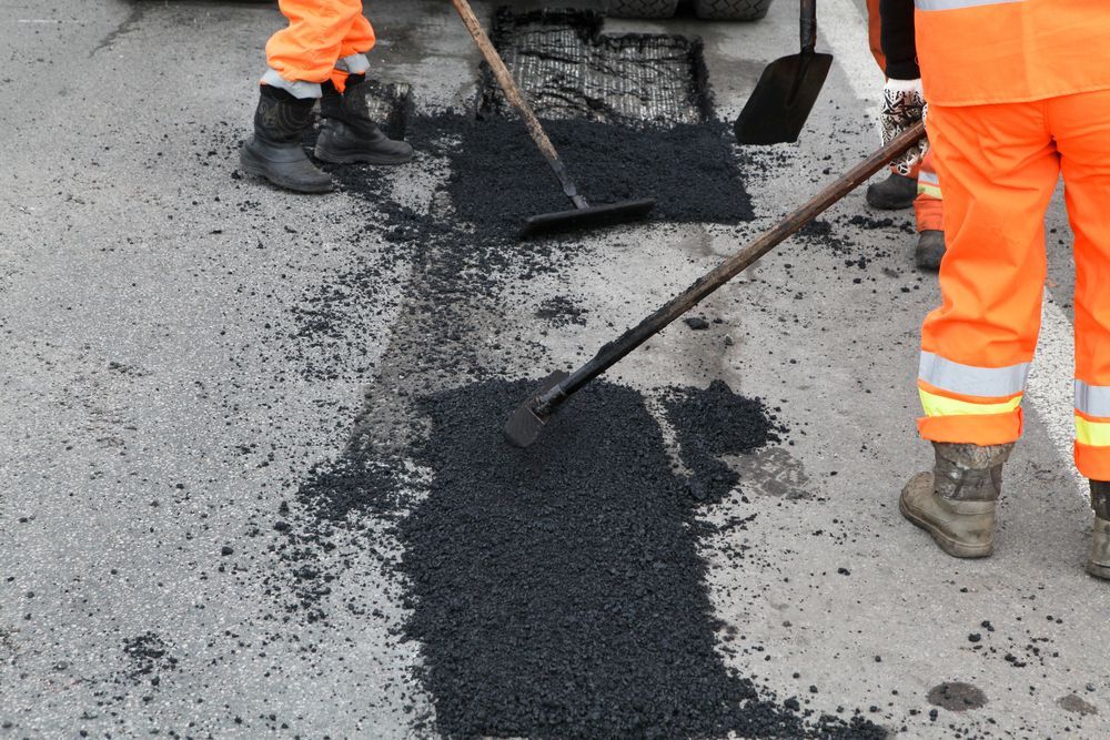 A Man is Spreading Asphalt on the Ground With a Shovel — F & J Bitumen Services in Katherine, NT