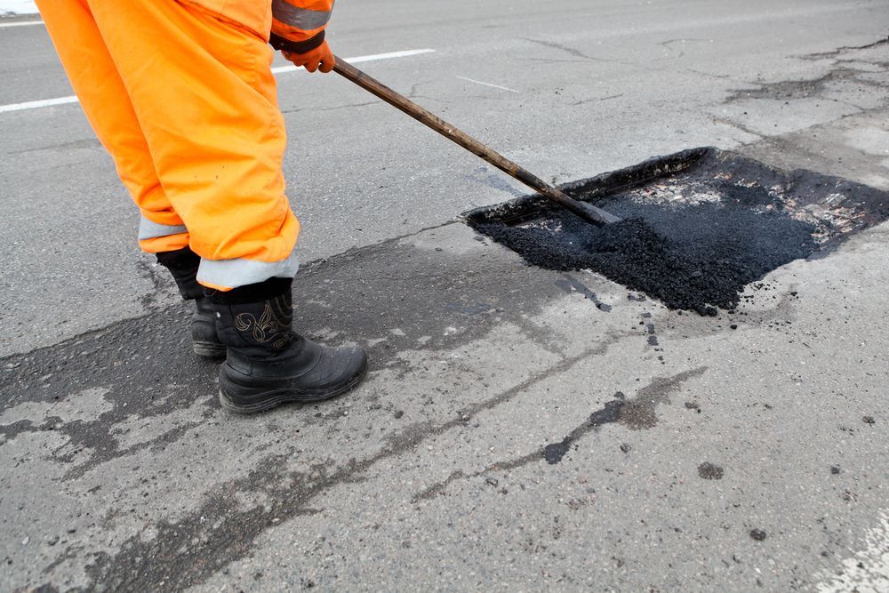 A Man is Spreading Asphalt on a Road With a Broom — F & J Bitumen Services in Alice Springs, NT