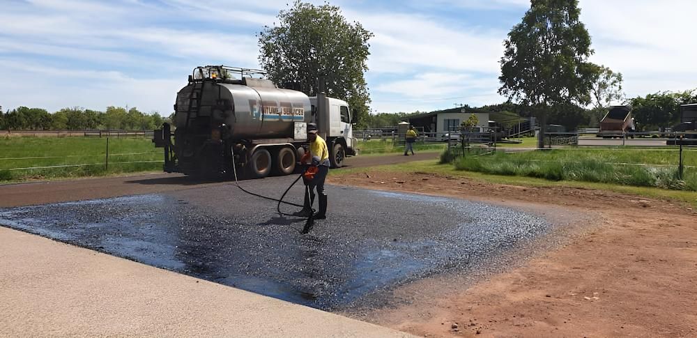 A Man is Spraying Asphalt on a Road Next to a Truck — F & J Bitumen Services in Humpty Doo, NT