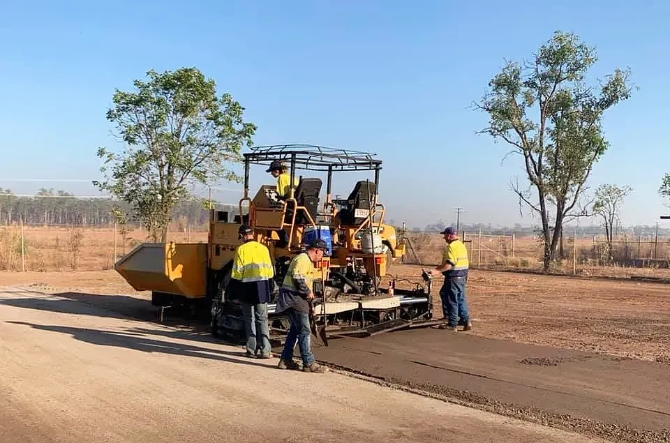 A Man is Laying Asphalt on a Driveway in Front of a House — F & J Bitumen Services in Humpty Doo, NT