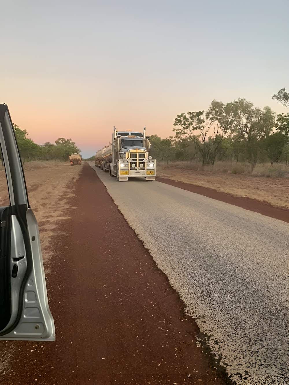 A Truck is Driving Down a Dirt Road Next to a Car — F & J Bitumen Services in Humpty Doo, NT