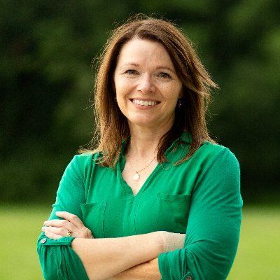 Photo of Christina Bohannan, a white woman with brown hair smiling while wearing a kelly green blouse, arms crossed in front of her