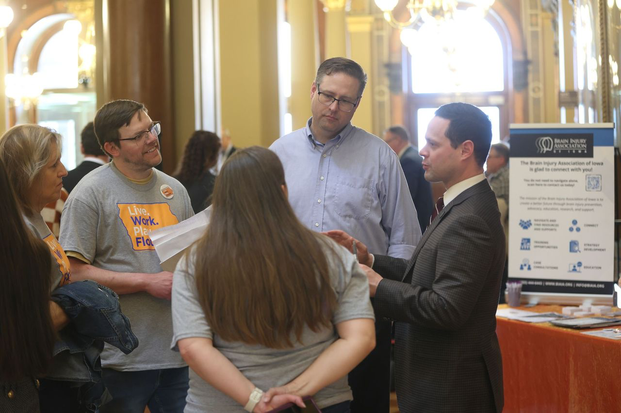 Carlyn Crowe, George Thompson, Kevin Harris, and Wendy Anderson talk to Sen. Matt Blake in front of a display booth at the State Capitol. 