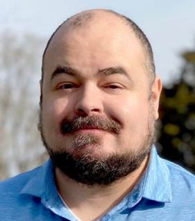 Photo of Ryan Melton, a smiling white man with a dark beard wearing a light blue dress shirt.