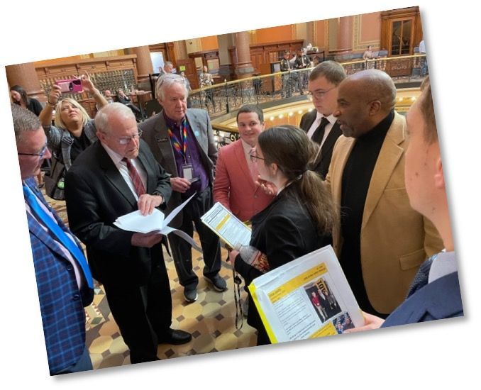Advocates holding papers are talking to a Senator and other legislators (who are looking at the paper) in the Capitol rotunda.