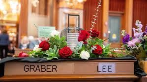 Photo of Rep. Graber's desk at the Capitol covered in red roses and purple flowers