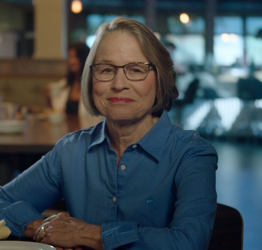 Photo of Mariannette Miller-Meeks, a smiling light-haired woman with glasses and wearing a blue shirt in a cafe.