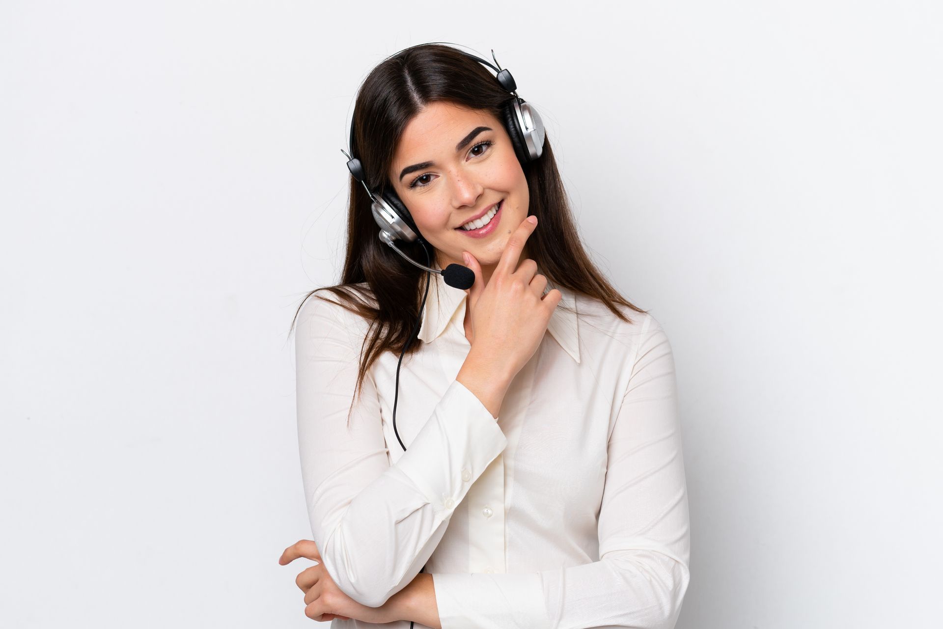 Mulher com fone de ouvido sorrindo, mão no queixo, contra um fundo branco.