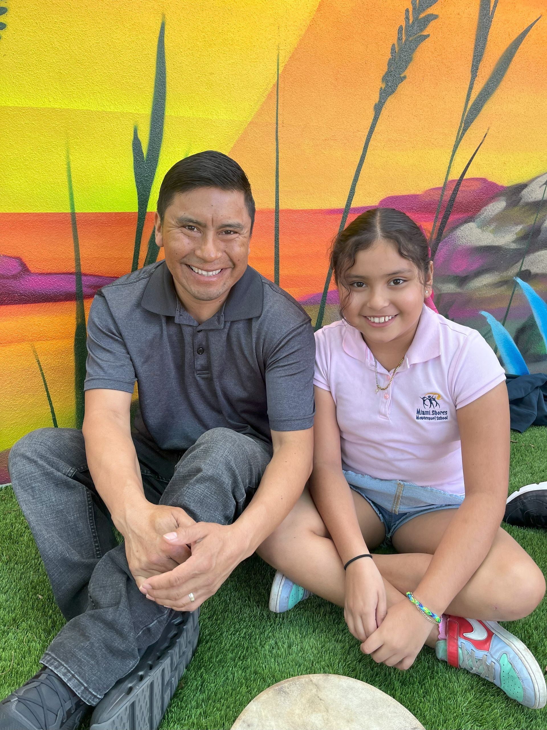 A Montessori parent and his child are sitting next to each other on the grass.