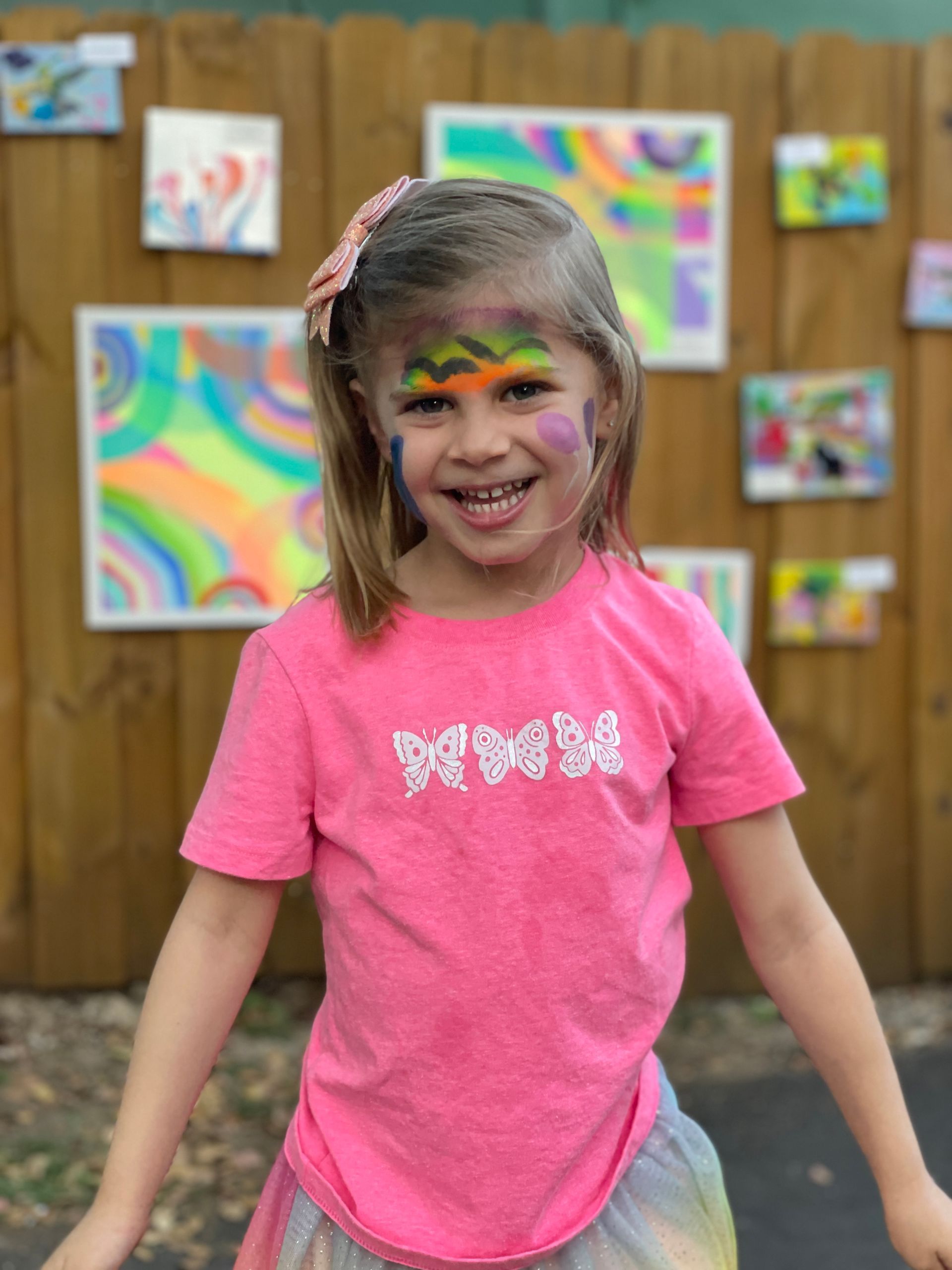 A Montessori child with her face painted in front of a wall of paintings