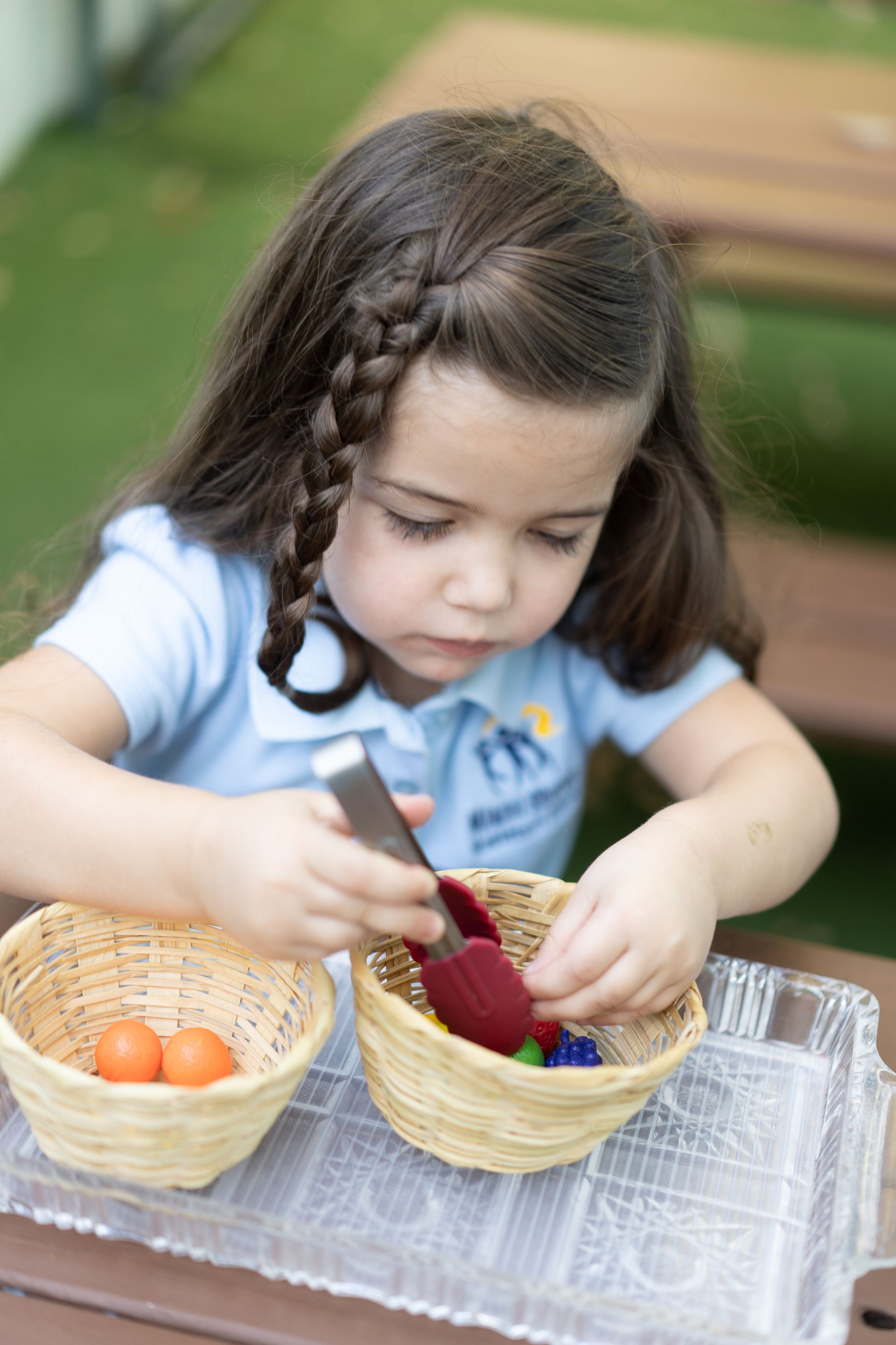 A Montessori child is sitting at a table working with baskets and spoons.