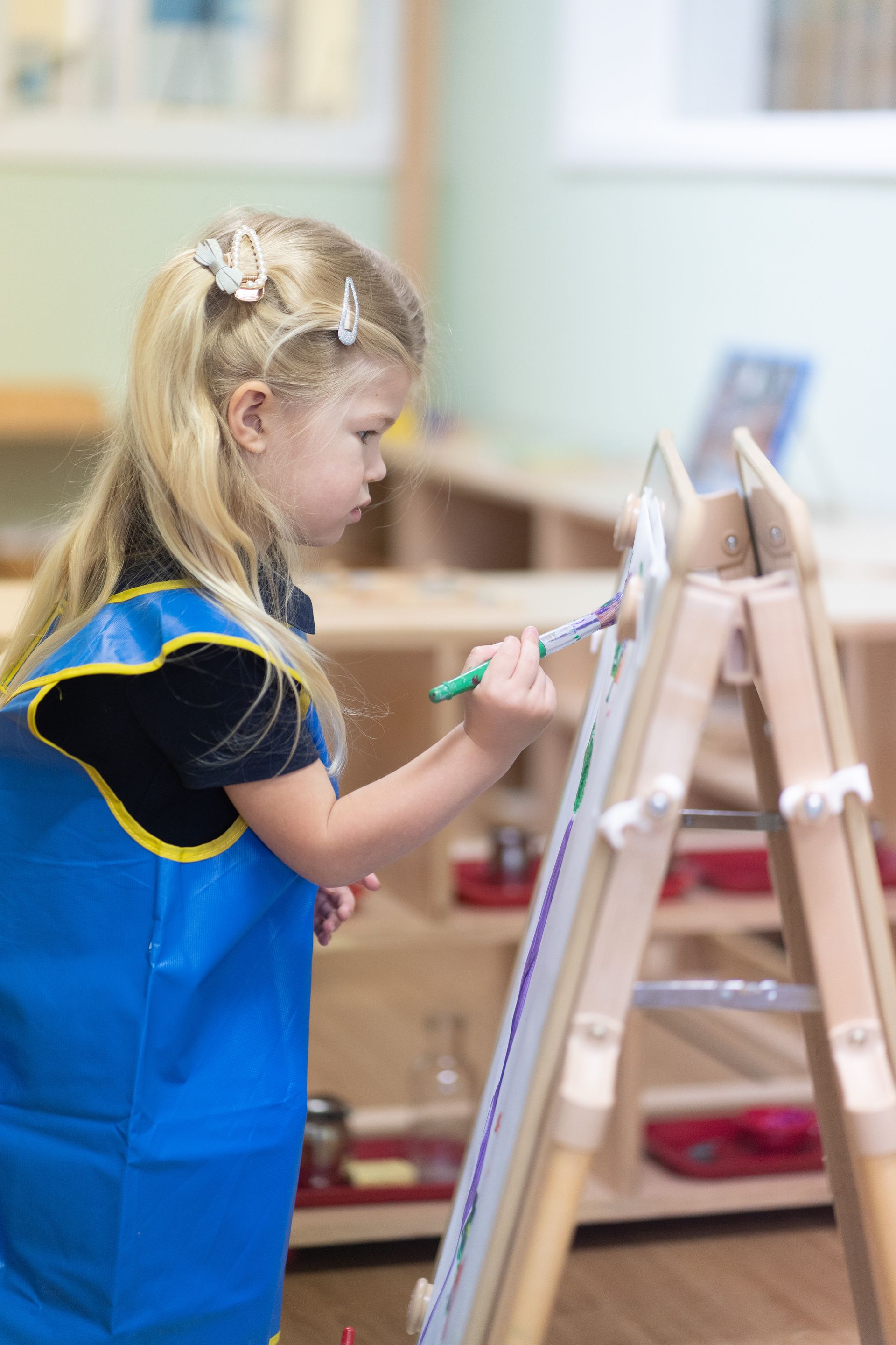A Montessori child is painting on an easel in a classroom.