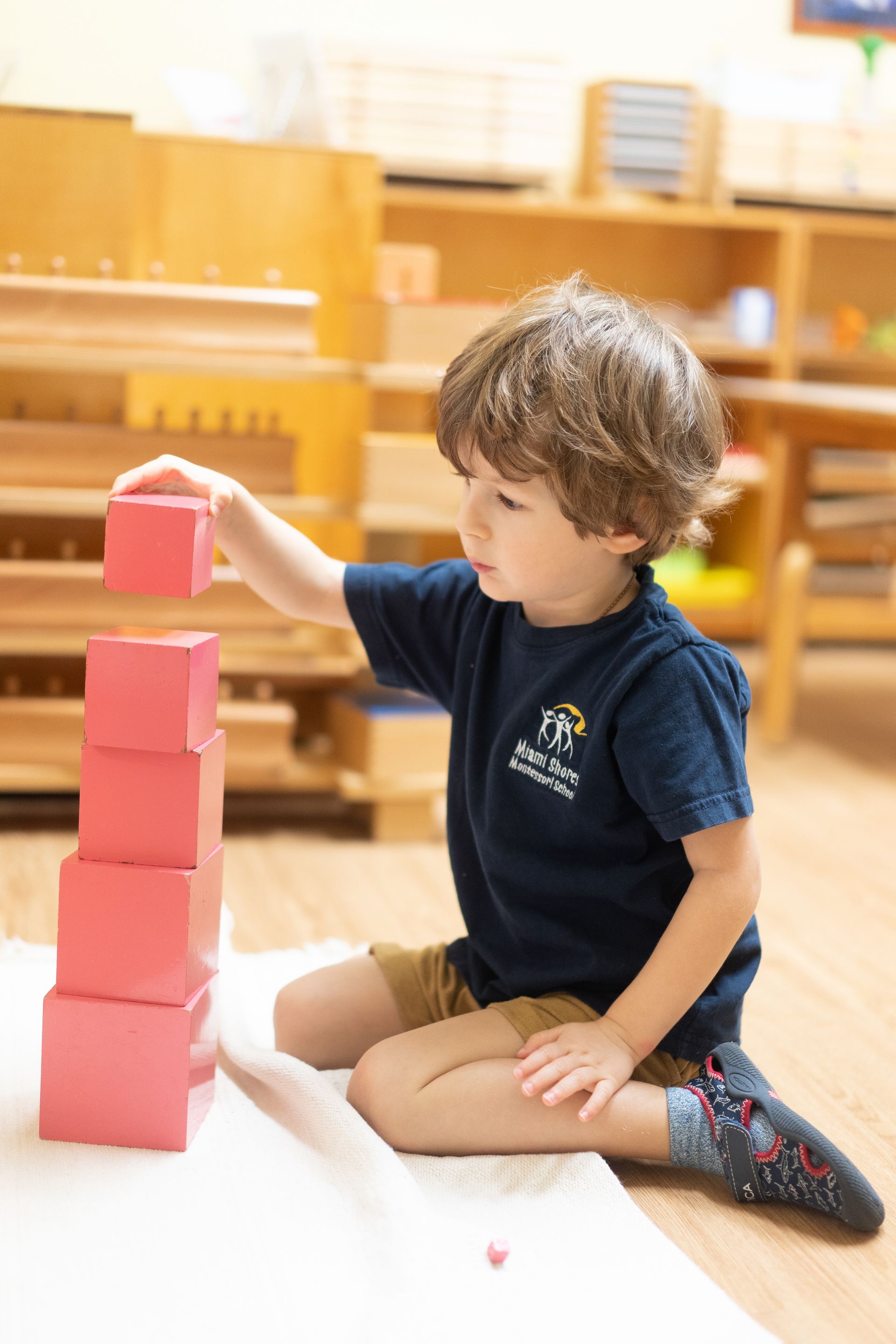 A Montessori child is sitting on the floor working with pink blocks.